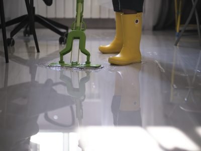 young boy in yellow rubber boots diligently cleaning up the aftermath of a flood in his apartment